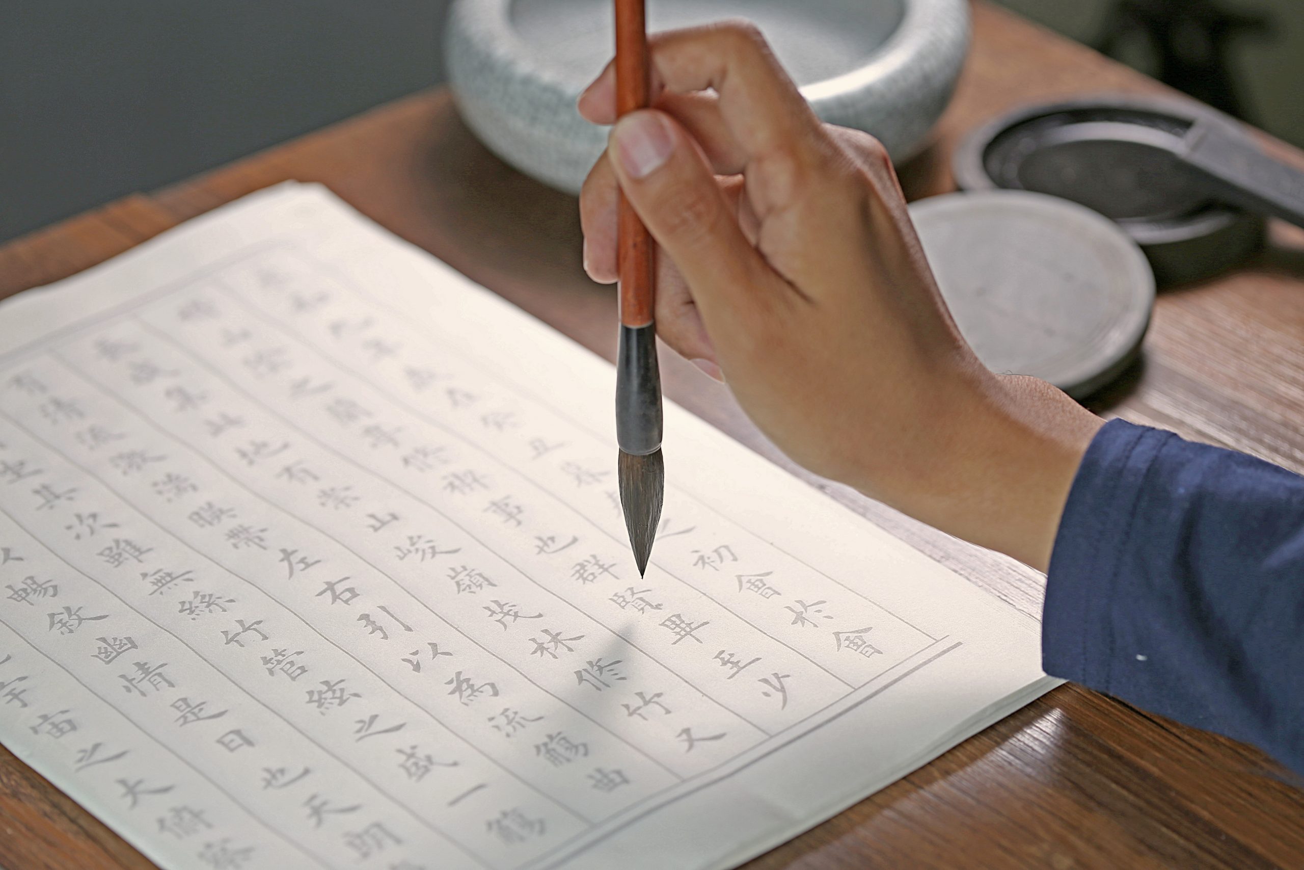Person practicing Chinese calligraphy with brush and ink on traditional paper
